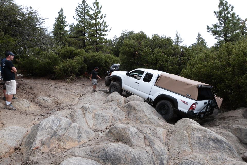 White Toyota pickup truck with tan camper shell navigating rocky terrain