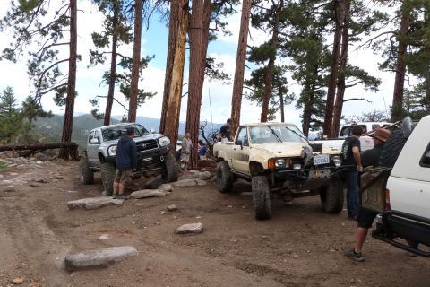 1985 Toyota 4Runner - Several modified trucks are parked on a rocky, wooded trail, suggesting an off-road excursion.
