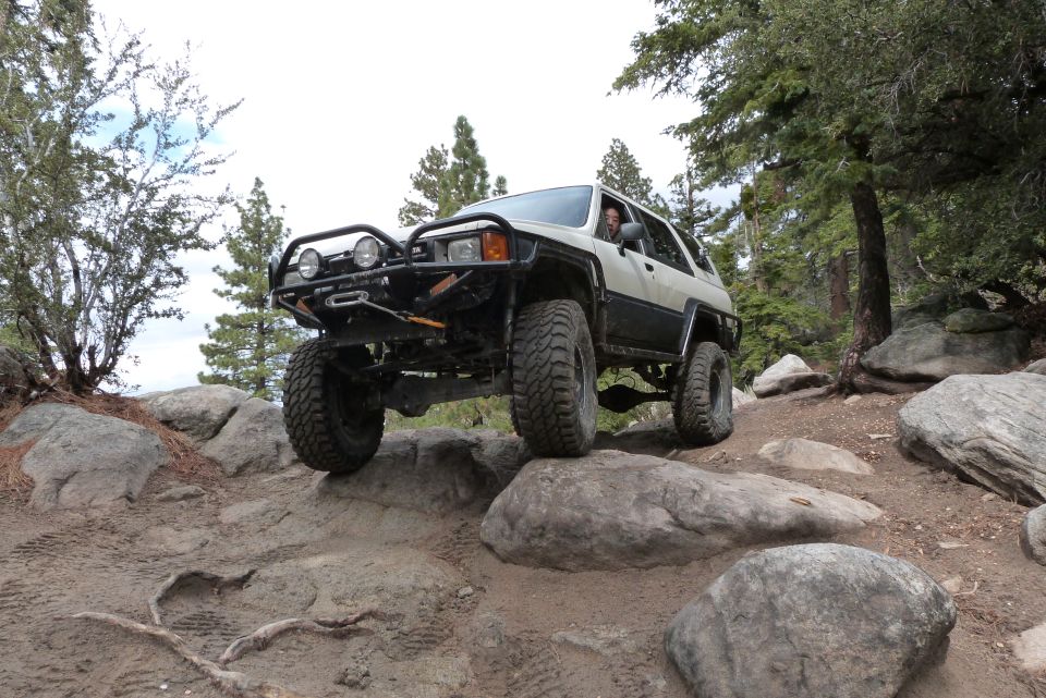 White and black Toyota 4Runner with off-road modifications navigating a rocky trail