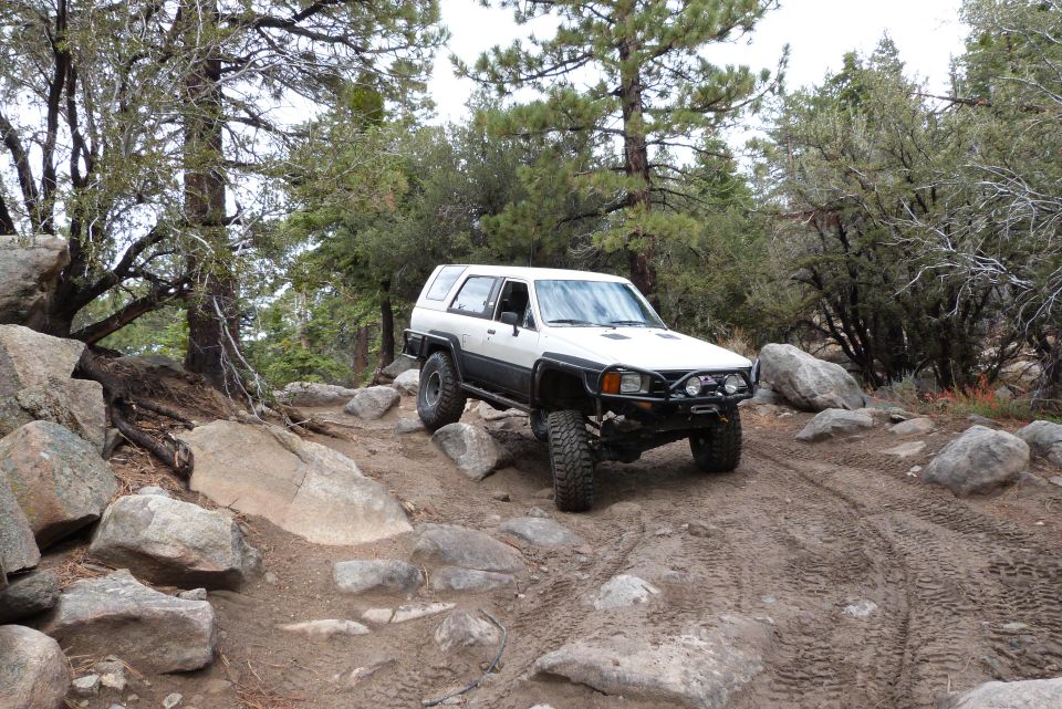 1985 Toyota 4Runner navigating a rocky off-road trail with trees and boulders