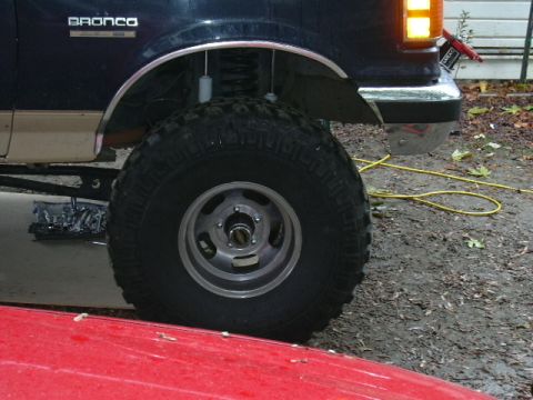 1991 Ford Bronco - Close-up of the front wheel and fender of a dark blue and tan two-tone Ford Bronco, showing the raised BRONCO badge on the front fender, a…