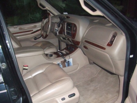 1996 Ford Bronco - The interior of a vehicle shows tan leather seats and a dashboard with wood trim accents.