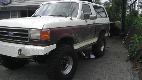 1989 Ford Bronco - This lifted Ford Bronco is parked outside a building with a basketball hoop visible.