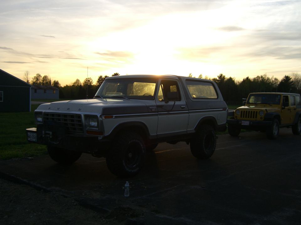 Two-tone 1978 Ford Bronco parked next to a yellow Jeep Wrangler during sunset
