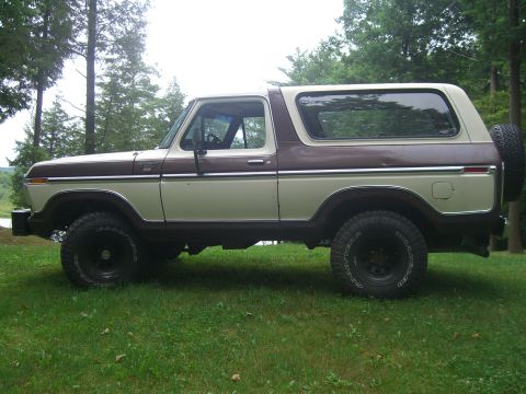1979 Ford Bronco - A two-tone brown and beige Ford Bronco is parked on a grassy lawn with trees in the background.