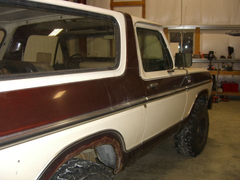 1979 Ford Bronco - Side view of a classic Ford Bronco, parked indoors with visible rust on the lower body panels.