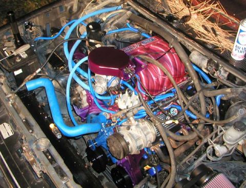 1988 Ford Bronco - Close overhead shot of an EFI V8 engine bay with a candy-red painted upper intake manifold and oval air-cleaner lid, purple-anodized bracke…