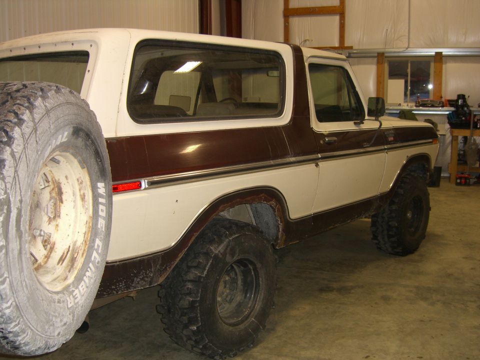 White and brown Ford Bronco with spare tire mounted on the back. It's in a garage