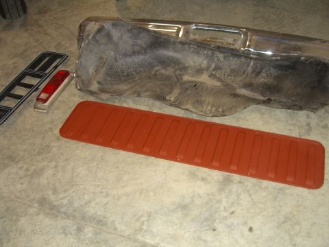 1979 Ford Bronco - Car parts including a bumper, tailgate trim, and taillight bezel are laid out on a concrete surface.