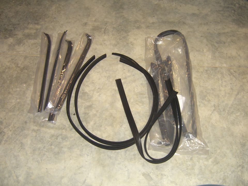 Several rubber seals and black trim pieces laid out on a concrete floor, some in plastic packaging