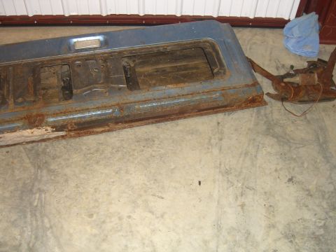 1979 Ford Bronco - A rusty blue tailgate interior and its latch mechanism are shown on a concrete floor next to a blue cloth.