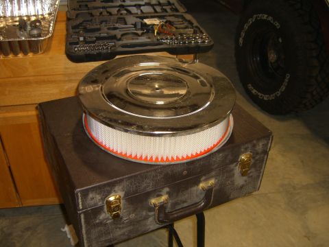 1979 Ford Bronco - A chrome air cleaner assembly sits atop a vintage suitcase, with a tire and tool case nearby.