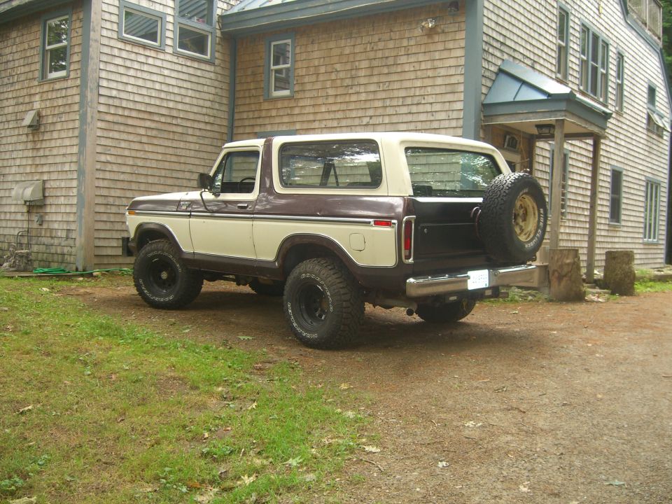 1979 Ford Bronco parked in front of a shingled house, rear-mounted spare tire visible
