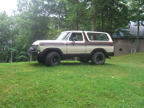 1979 Ford Bronco - This two-tone brown and cream 1978 Ford Bronco features off-road tires and is parked on a grassy incline with trees and a house in the back…
