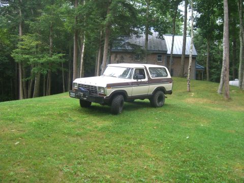 1979 Ford Bronco - This 1979 Ford Bronco is parked on a grassy slope with a wooded area and house in the background.