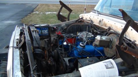 1979 Ford Bronco - The engine bay of a vehicle, a blue Ford engine and an Exide battery, with a Supermotors logo visible.
