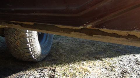1979 Ford Bronco - A close-up view of a vehicle's lower body panel shows rust and damage, with an off-road tire partially visible.