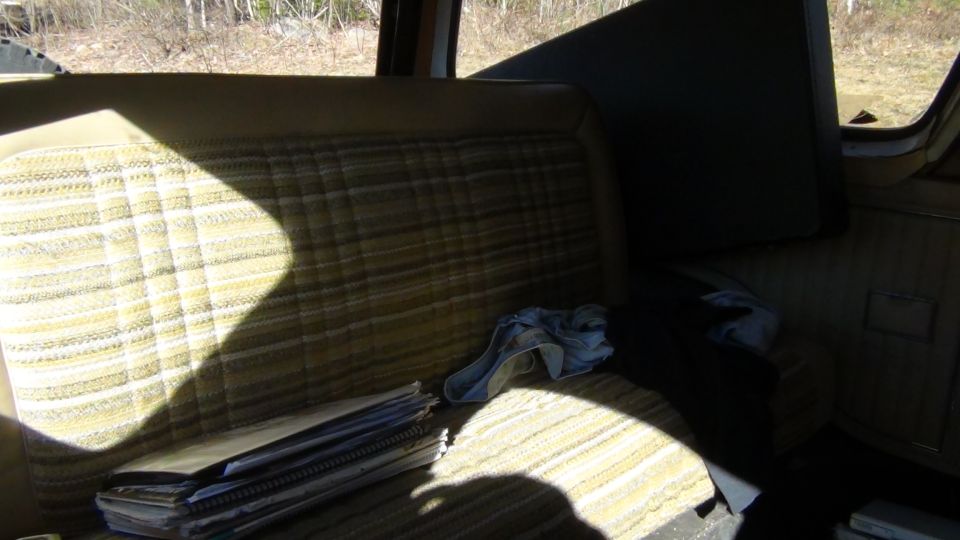 Vehicle interior showing plaid patterned bench seat with a stack of papers and a cloth on it