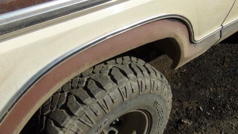 1979 Ford Bronco - Close-up of a vehicle's wheel well and tire, showing off-road tread and tan paint with brown trim.