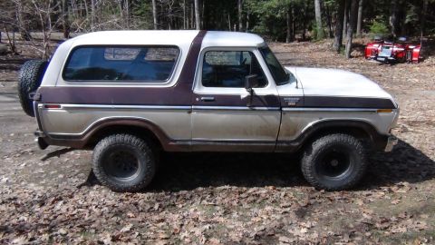 1979 Ford Bronco - This Ford Bronco is parked outdoors on a dirt and leaf-covered surface.