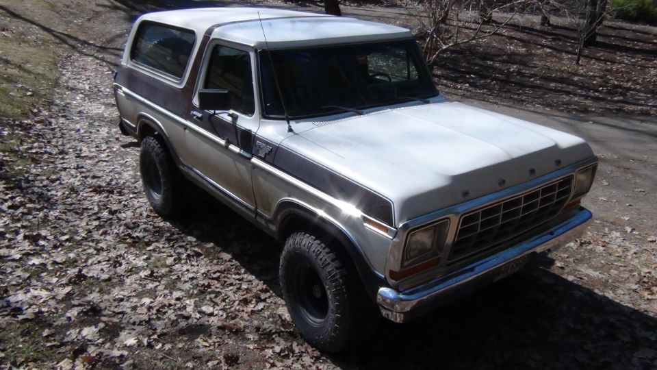 White and brown Ford Bronco with aftermarket wheels parked on a dirt road