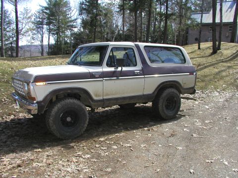 1979 Ford Bronco - This two-tone Ford Bronco is parked on a dirt road with a wooded area and house visible.
