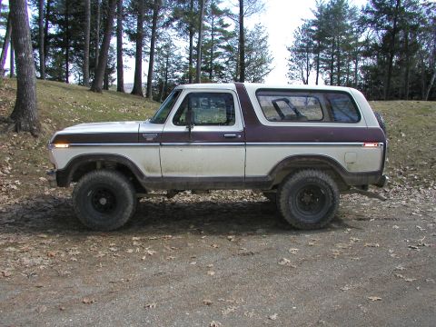 1979 Ford Bronco - A side view of a classic Ford Bronco, likely from the late 1970s, sits on a dirt path surrounded by trees.