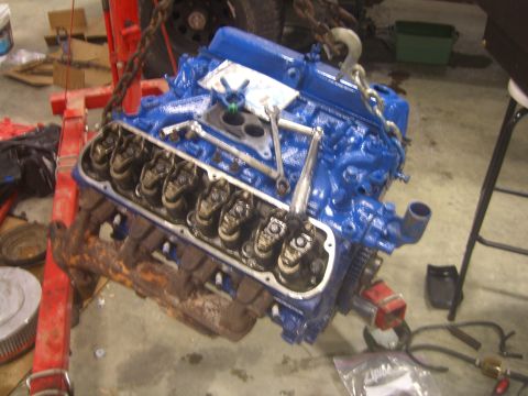 1979 Ford Bronco - A blue V8 engine is suspended by a red engine hoist, with its valve covers removed, revealing internal components.