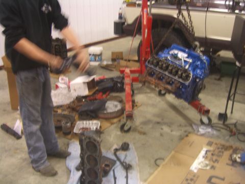 1979 Ford Bronco - Engine assembly and parts laid out in a garage, with a person working in the background.