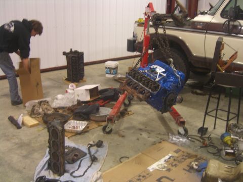 1979 Ford Bronco - A person works on an engine in a garage, with another engine and a truck visible.