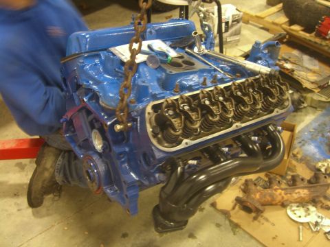1979 Ford Bronco - A blue V8 engine is being hoisted, revealing its internal components and black headers.