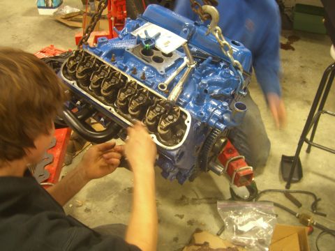1979 Ford Bronco - A person works on a blue engine that is suspended by chains in a garage.