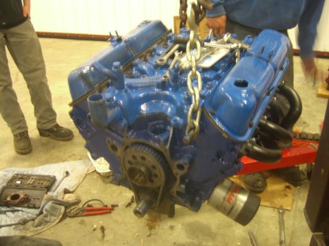 1979 Ford Bronco - A blue V8 engine is suspended by chains, with tools and an oil filter nearby on the ground nearby.