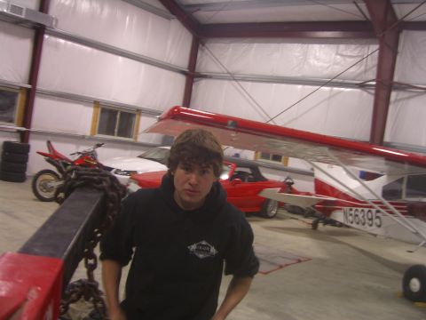 1979 Ford Bronco - A man stands in a hangar near a red convertible and a small airplane.