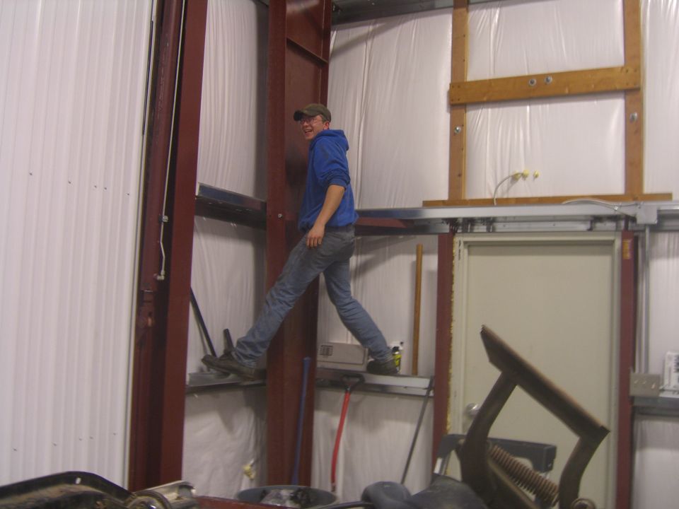 Guy in blue hoodie and jeans walking on metal beams inside a garage