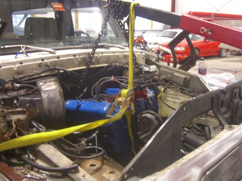 1979 Ford Bronco - Engine bay of a vehicle being worked on, with an engine hoist attached and another car in the background.