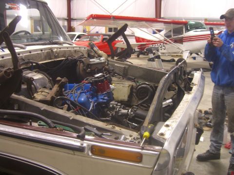 1979 Ford Bronco - The engine bay of a truck is open for inspection, with a person in the background holding a phone.