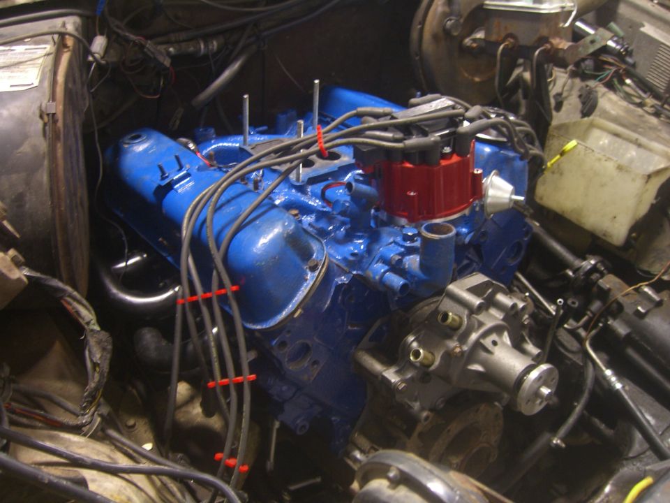 Engine bay with a blue engine, red distributor cap, and various hoses and wires