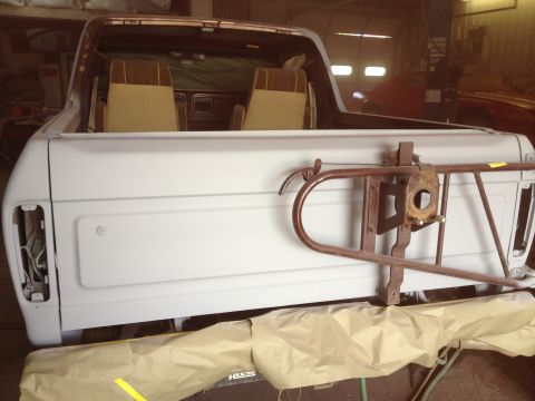 1979 Ford Bronco - Rear view of a white 1978 Ford Bronco undergoing repairs, showing its interior and spare tire mount.