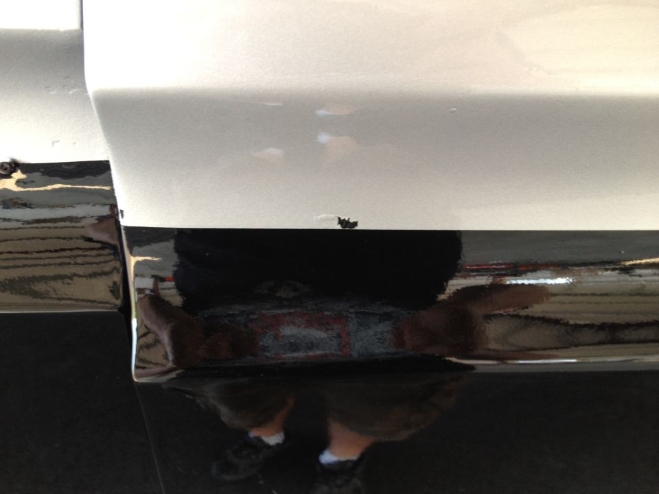 White and black vehicle lower body panel with chrome trim and reflection. Small chip on white paint