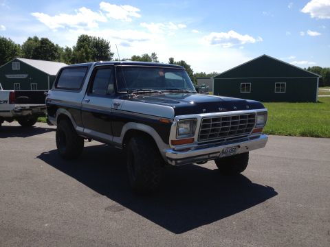 1979 Ford Bronco - This two-tone Ford Bronco is parked in front of a barn on a sunny day, with a pickup truck nearby.