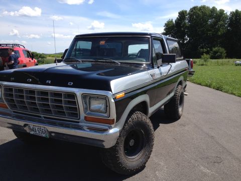 1979 Ford Bronco - A two-tone black and silver Ford Bronco is parked on a paved surface with a red SUV in the background.