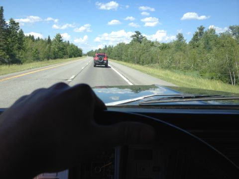 1979 Ford Bronco - Driving on a highway behind a red SUV on a sunny day with trees lining the road.