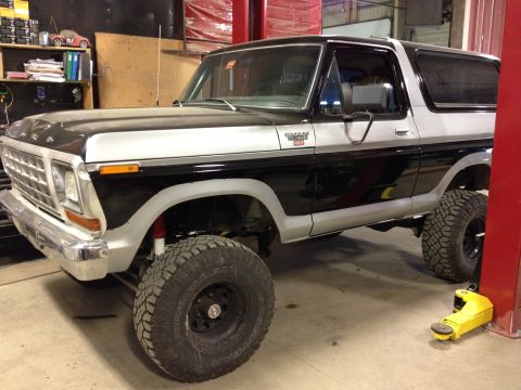 1979 Ford Bronco - A two-tone Ford Bronco with a lifted suspension is shown from a three-quarter front view in a garage setting.