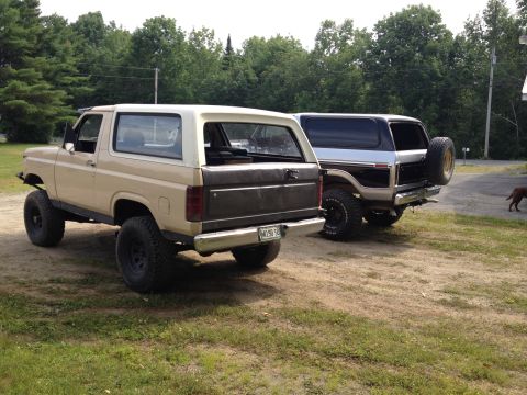 1979 Ford Bronco - Two 1979 Ford Broncos are parked side-by-side on a dirt lot with trees in the background.