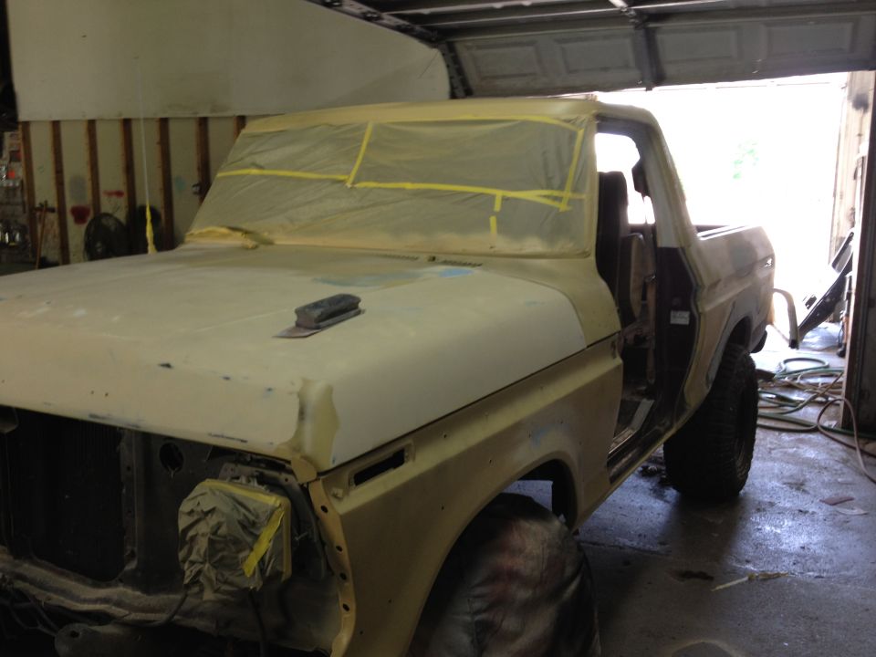 Yellow Ford Bronco in garage, masked for paint, with sanding block on hood