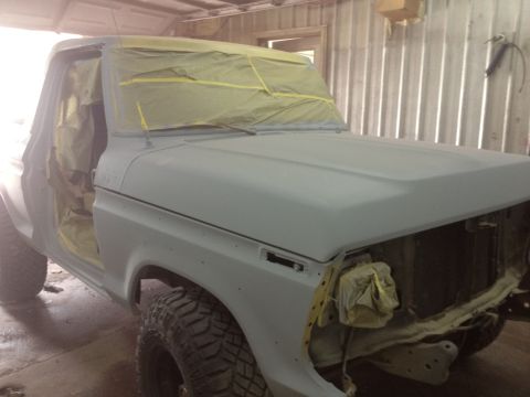 1979 Ford Bronco - A Ford truck in primer, with windows and doors taped off, sits in a workshop.