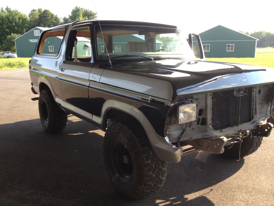 Ford Bronco with front end removed, parked outside two green buildings