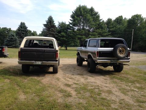 1979 Ford Bronco - Two Ford Broncos are parked outdoors on a dirt path with trees in the background.