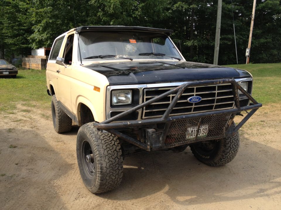 Tan Ford Bronco with black hood and a large metal bumper. License plate visible